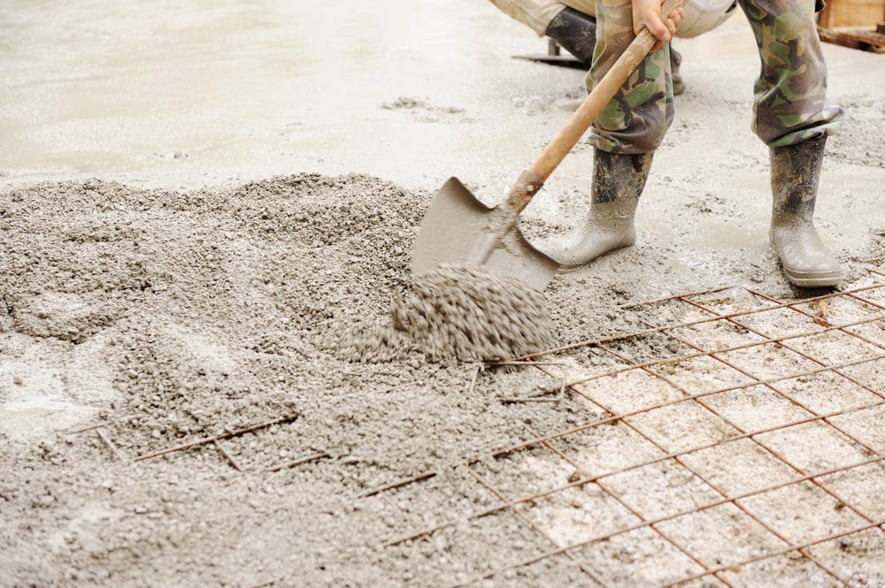 Construction worker shoveling wet concrete over a steel rebar grid during a slab pour